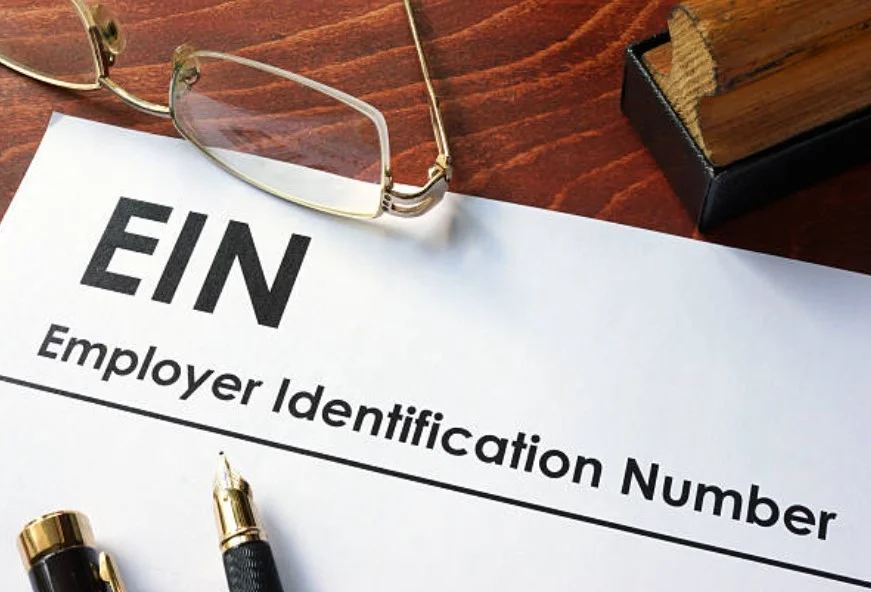 Bir gözlüg ve masada ir kağıt duruyor. Kağıt üzerinde bir dolmakalem kağıtta EIN yazıyor